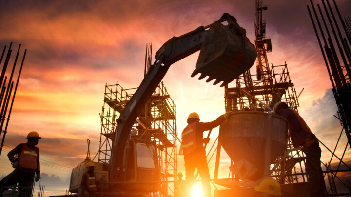 Construction workers with earth movers and a setting sun