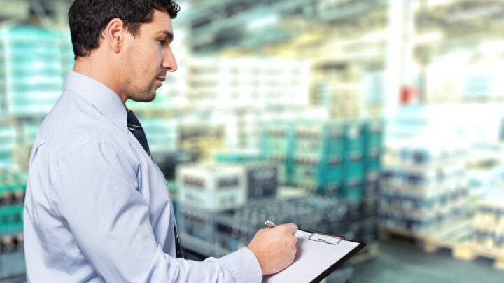 Engineer with a clipboard reviewing Professional standards in a warehouse or factory