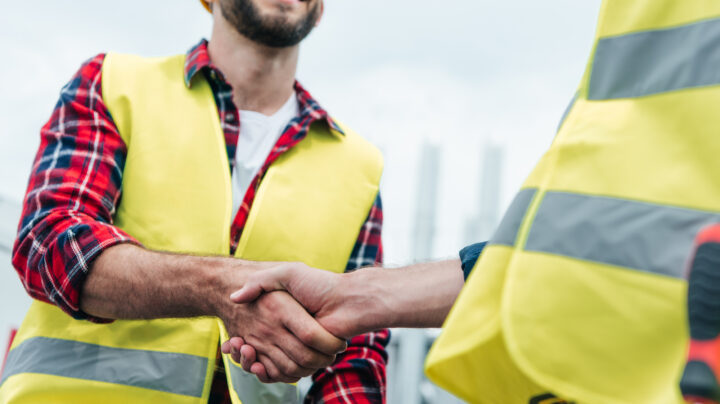 cropped view of engineers in safety vests shaking hands on roof