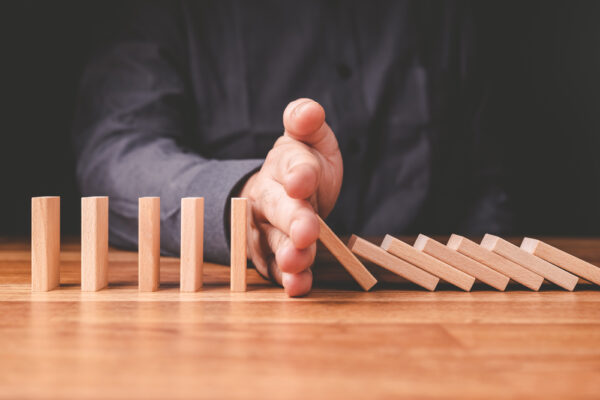 a hand sstopping a row of dominoes falling signifying risk management in supply and logistics